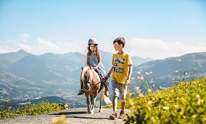 Mädchen reitet auf einem Pony und Bruder achtet auf sie.
