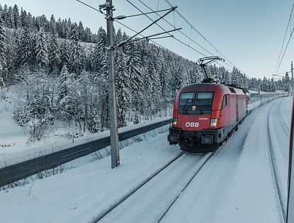 Roter Zug der ÖBB fährt im Winter durch Schnee auf den Schienen